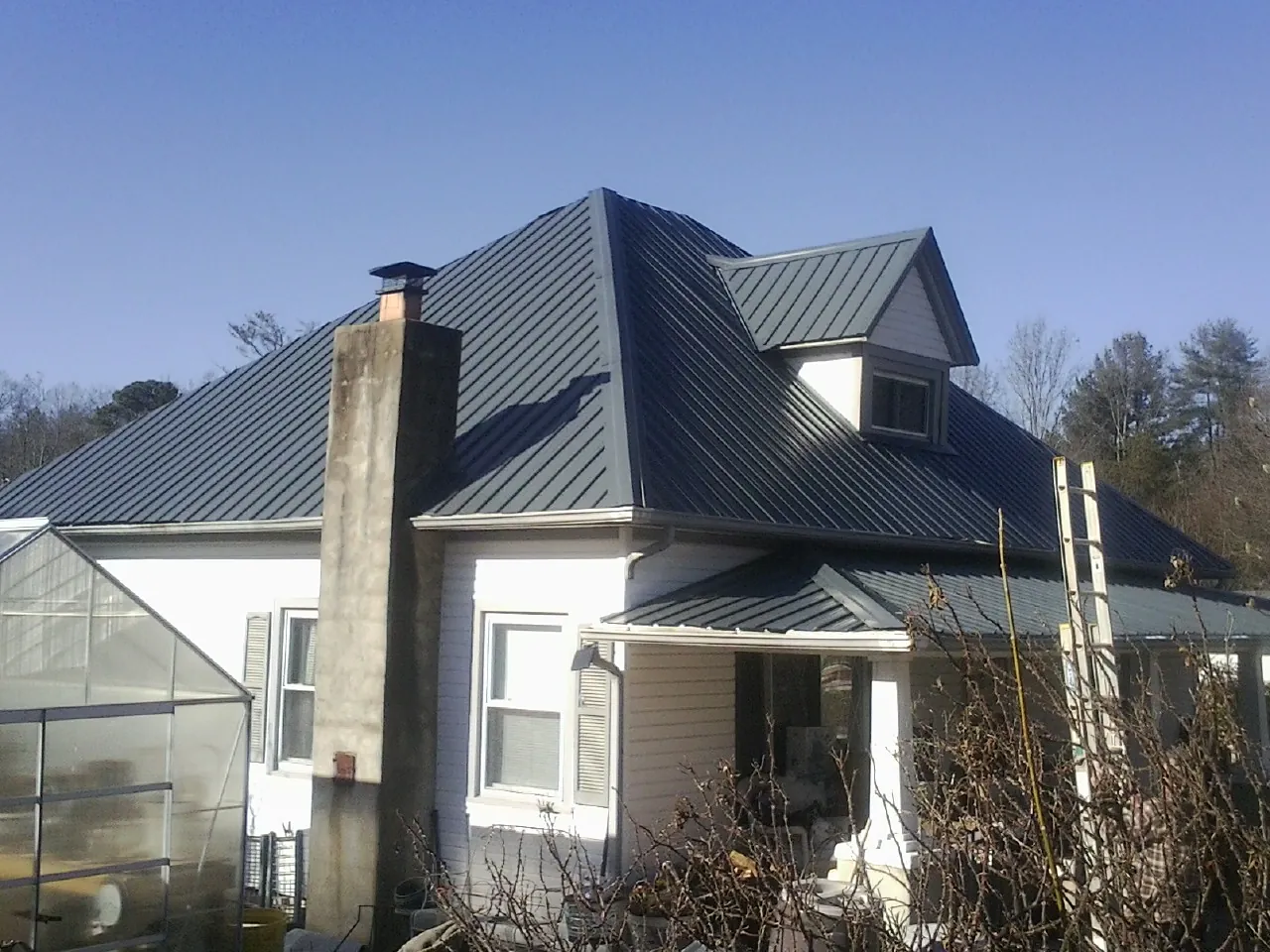Dark blue standing seam metal roof on a white farmhouse with dormer — Slate & Tile Roof Repair by Roofing Brothers in Bruno