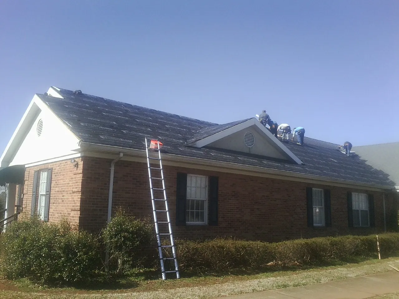 Crew tearing shingles off a brick ranch roof with a ladder set — Emergency Roof Repair work by our crew in Bruno