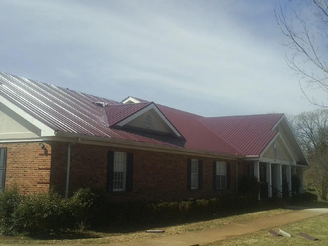 Red metal roof with gabled entries on a long brick building, from a Hail Damage Roof Repair job in Bruno