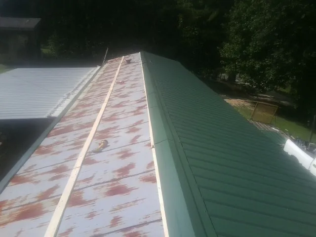 Old rusted panels beside newly installed green metal roofing — Wind Damage Roof Repair by Roofing Brothers in Bruno