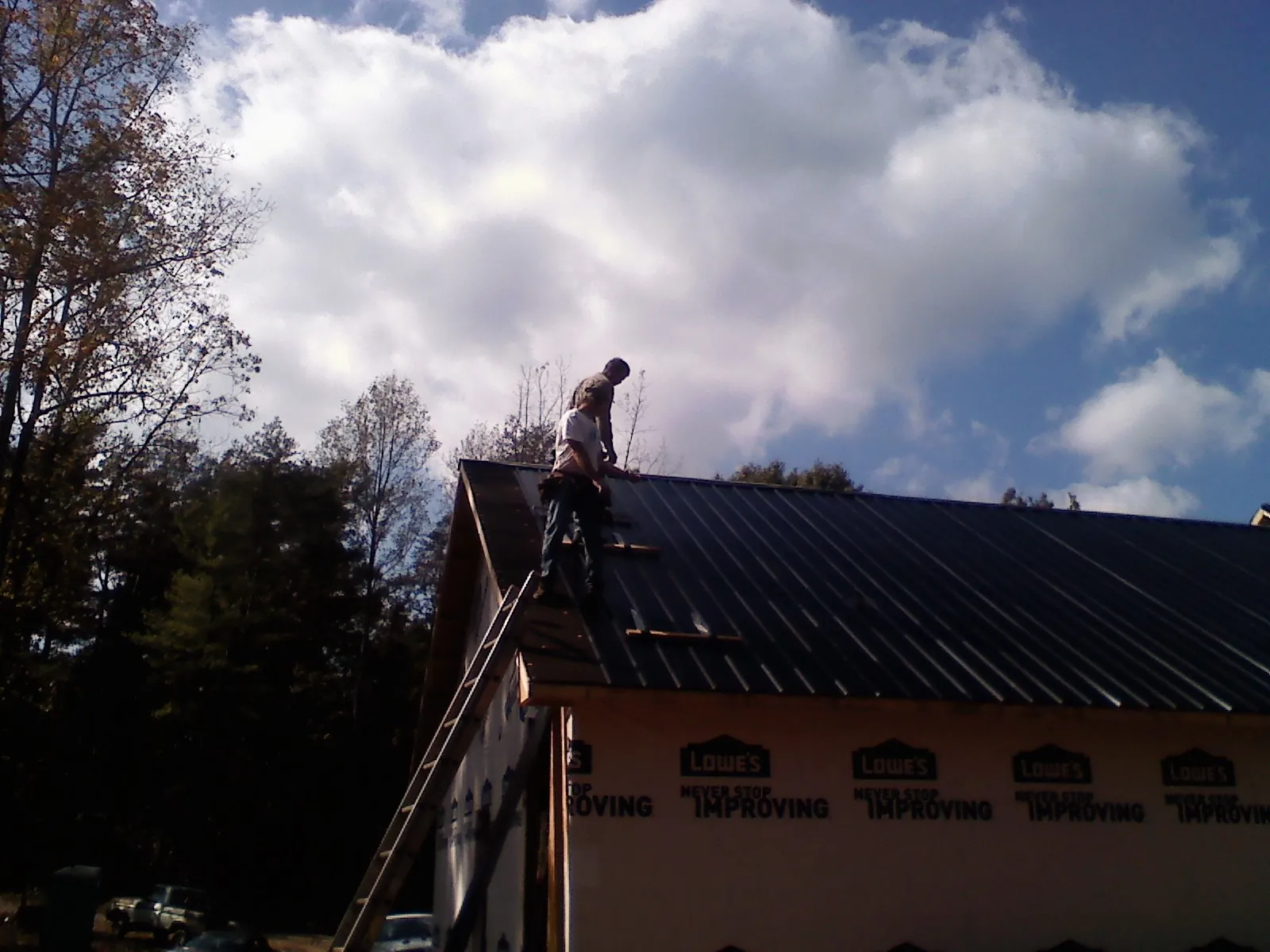 Roofer fastening dark metal panels high against a cloudy sky, from a Roof Inspection job in Bruno