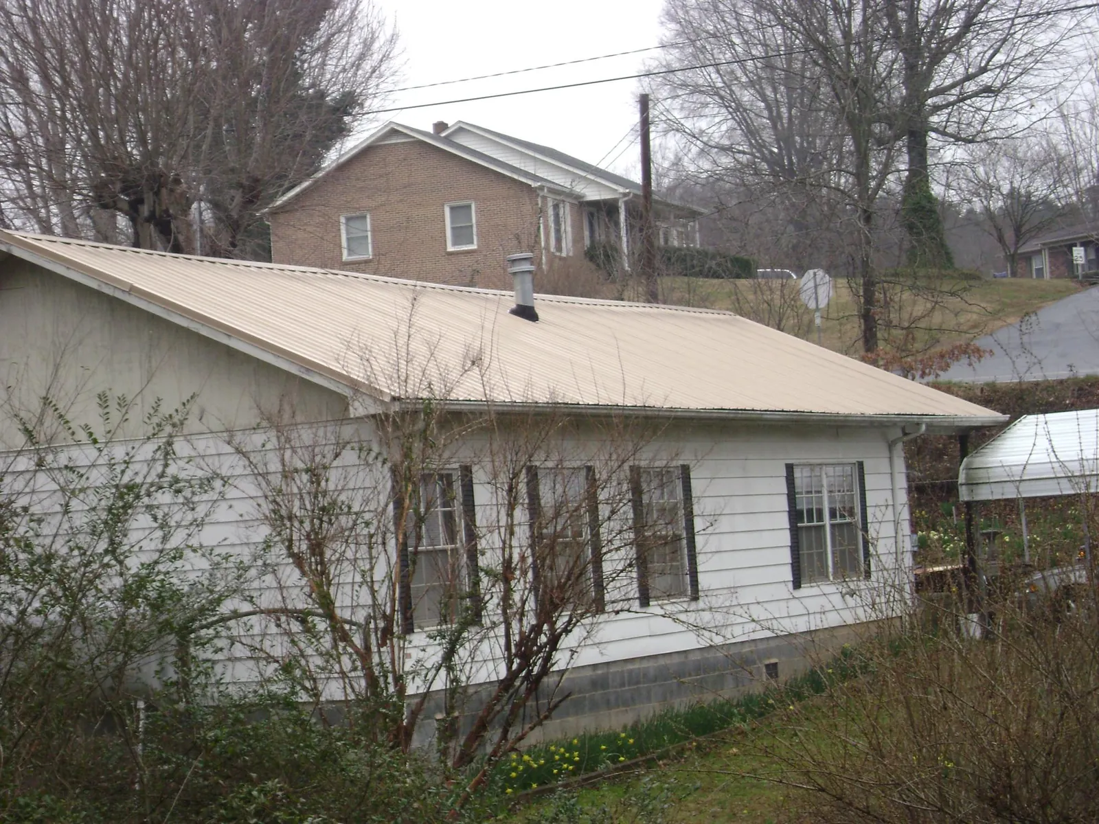 Tan metal roof on a white sided house set into a hillside — Commercial Roofing by Roofing Brothers in Bruno