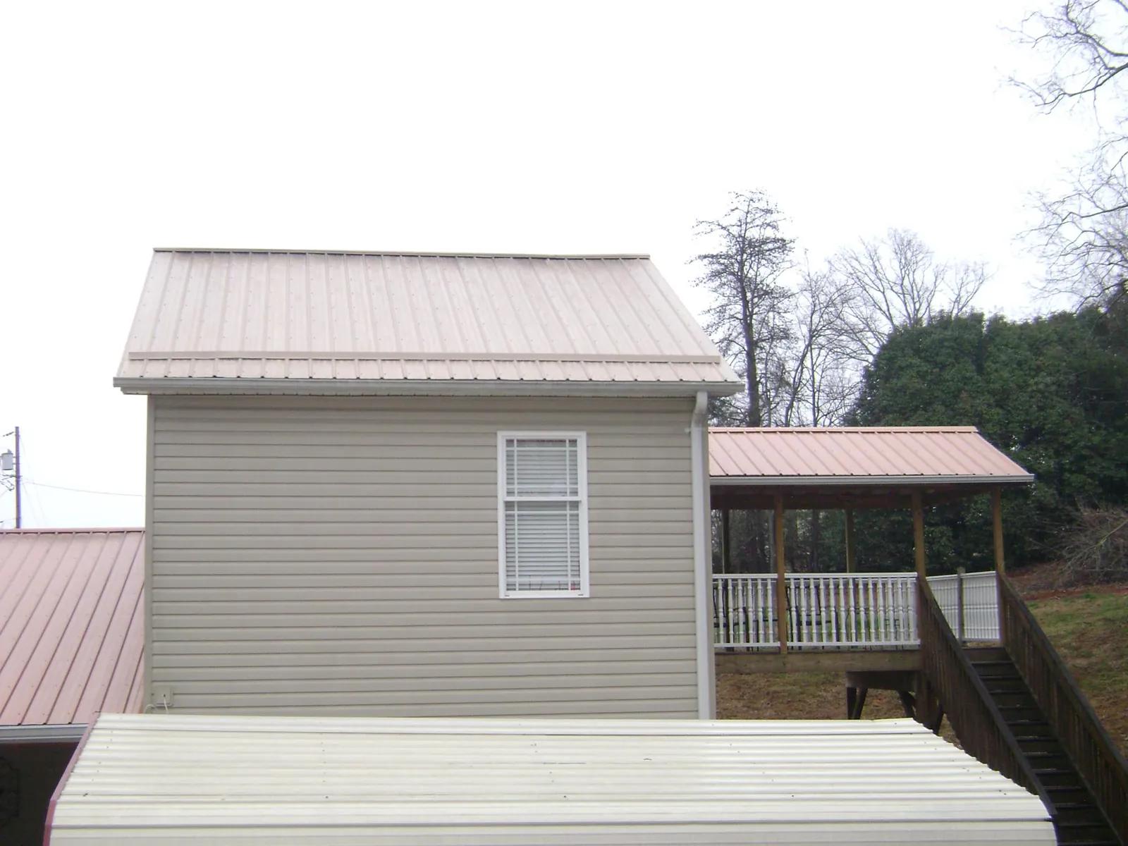 Tan metal roofs on a two story addition and attached porch, from a Roof Replacement job in Bruno